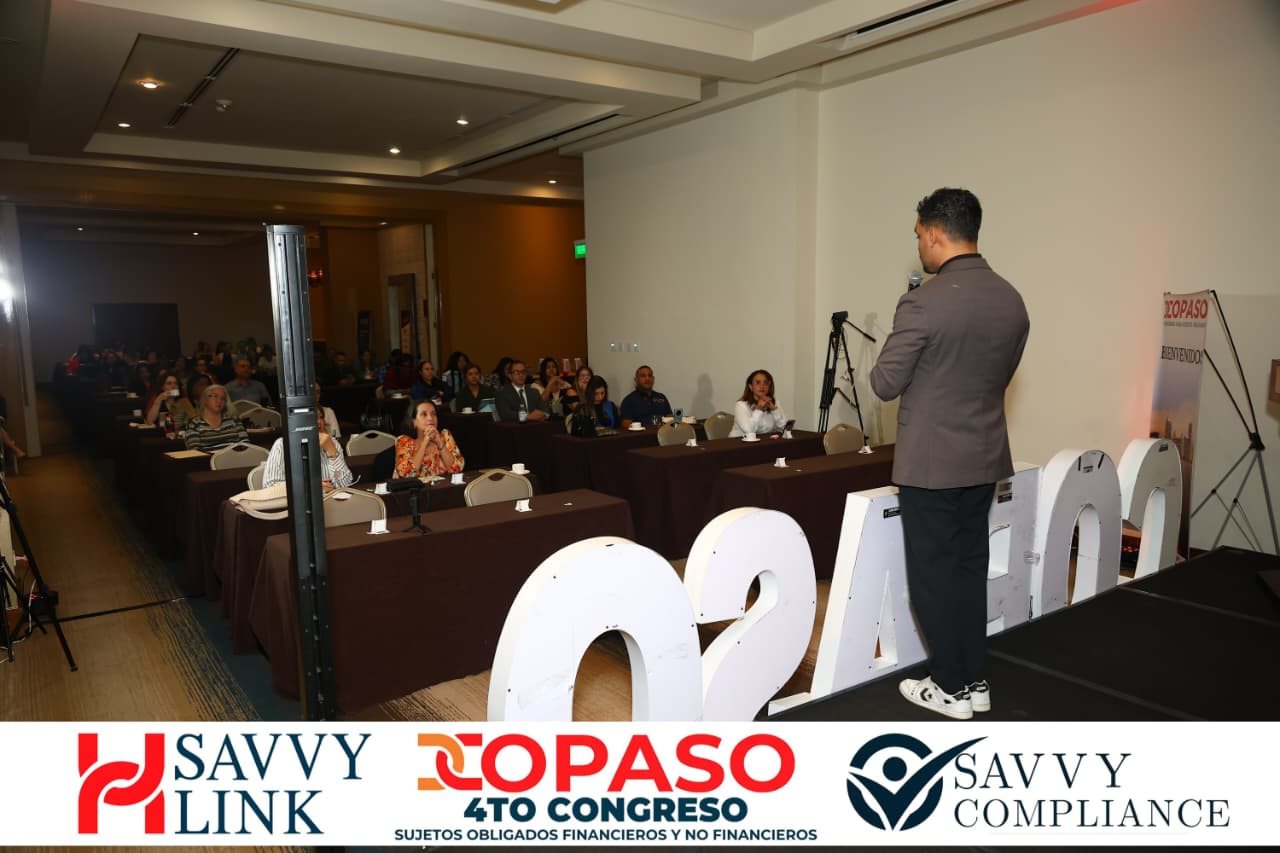 Chiragx standing on the COPASO 2026 stage, back to the camera, speaking with a microphone to the full room at the RIU Plaza Panamá, with the lit COPASO letters in front