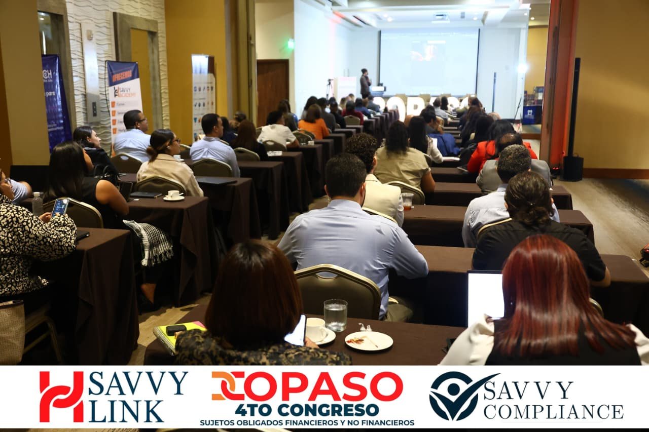 The COPASO 2026 room seen from the back, full of attendees at tables watching the stage screen where the site is being built live